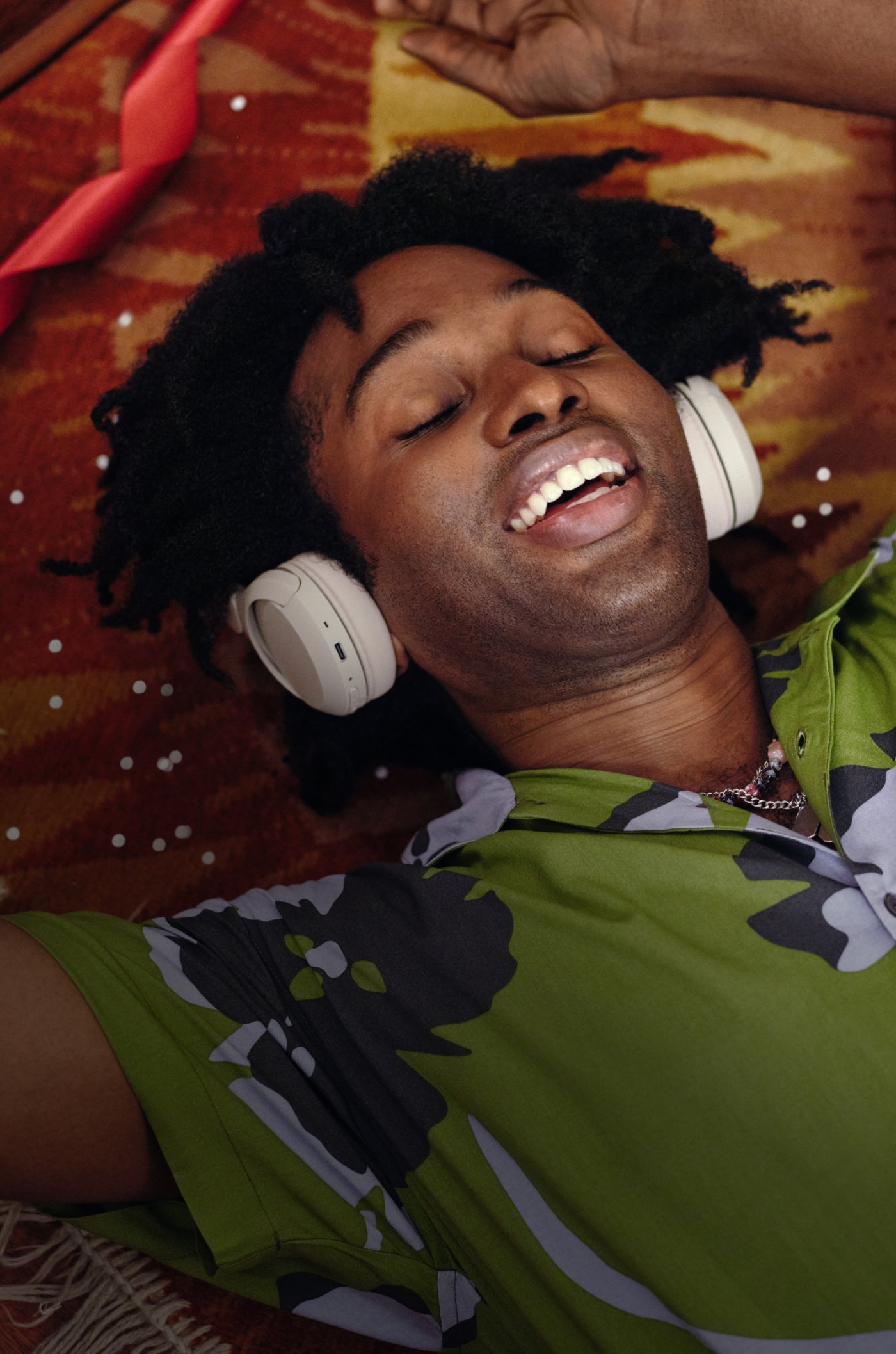 Person lying back on a patterned blanket wearing white over-ear headphones, laughing