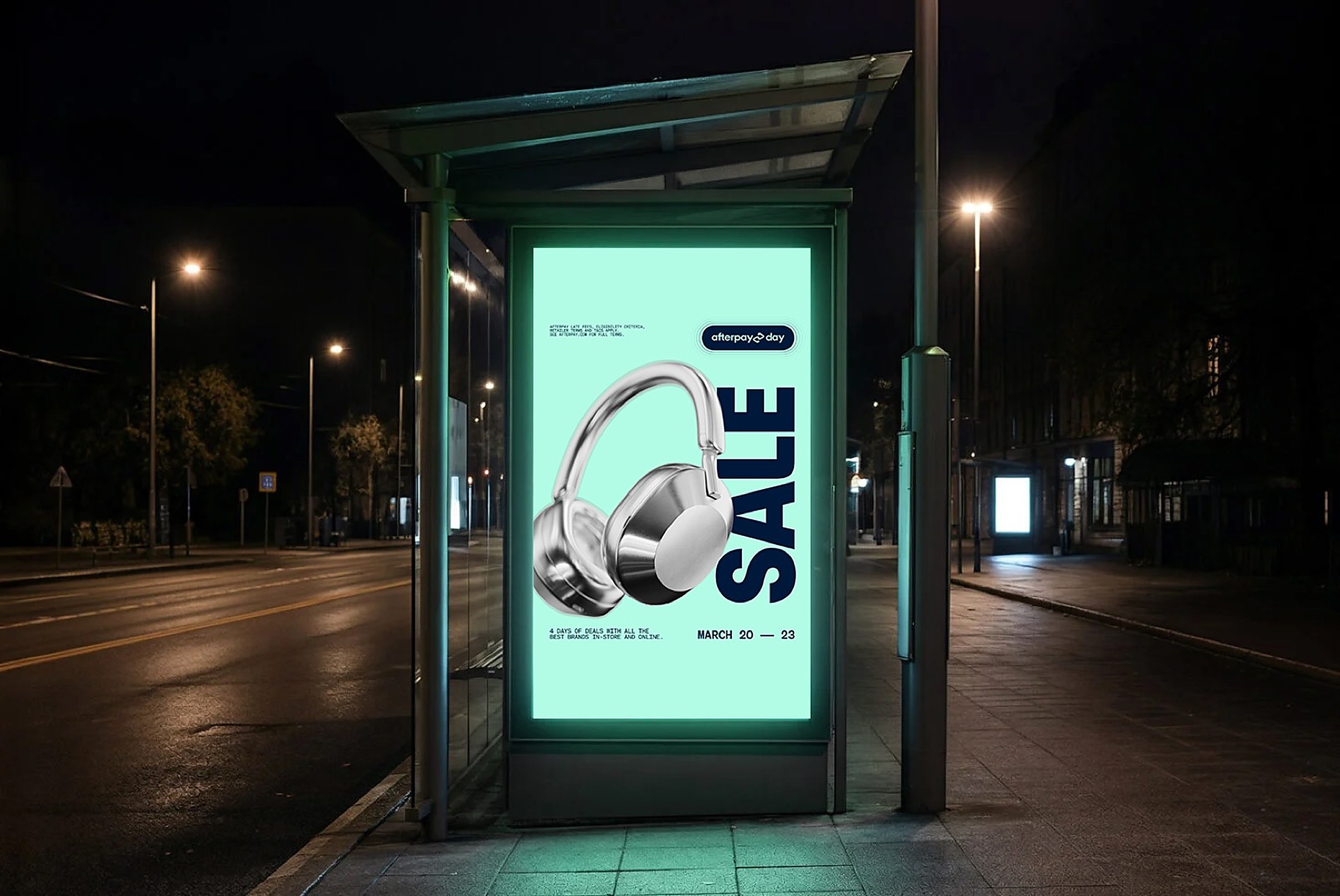 Lit bus shelter poster at night advertising an Afterpay sale, with white over-ear headphones