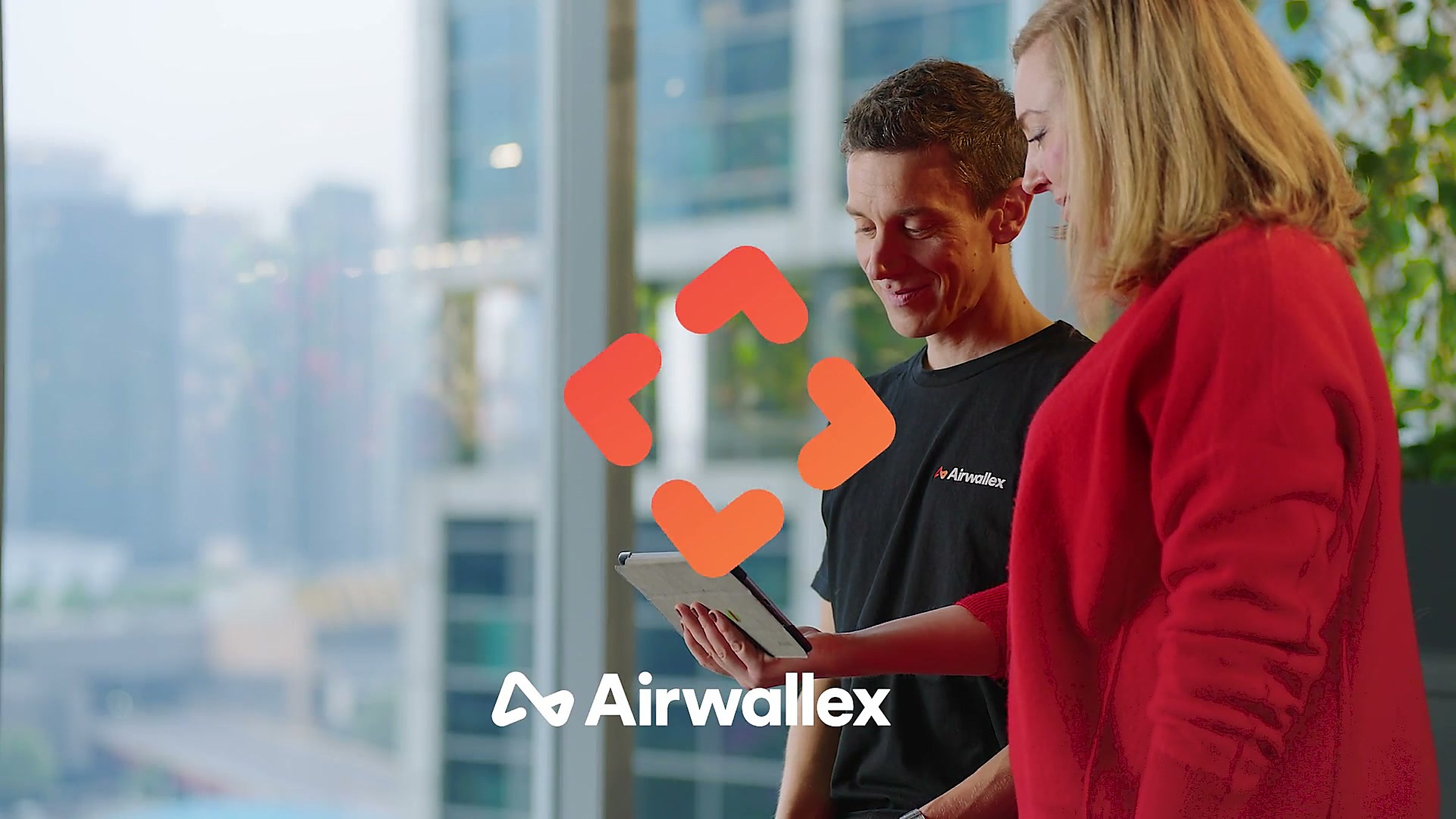 Airwallex brand film still: two colleagues looking at a tablet against a city skyline, Airwallex logo overlaid